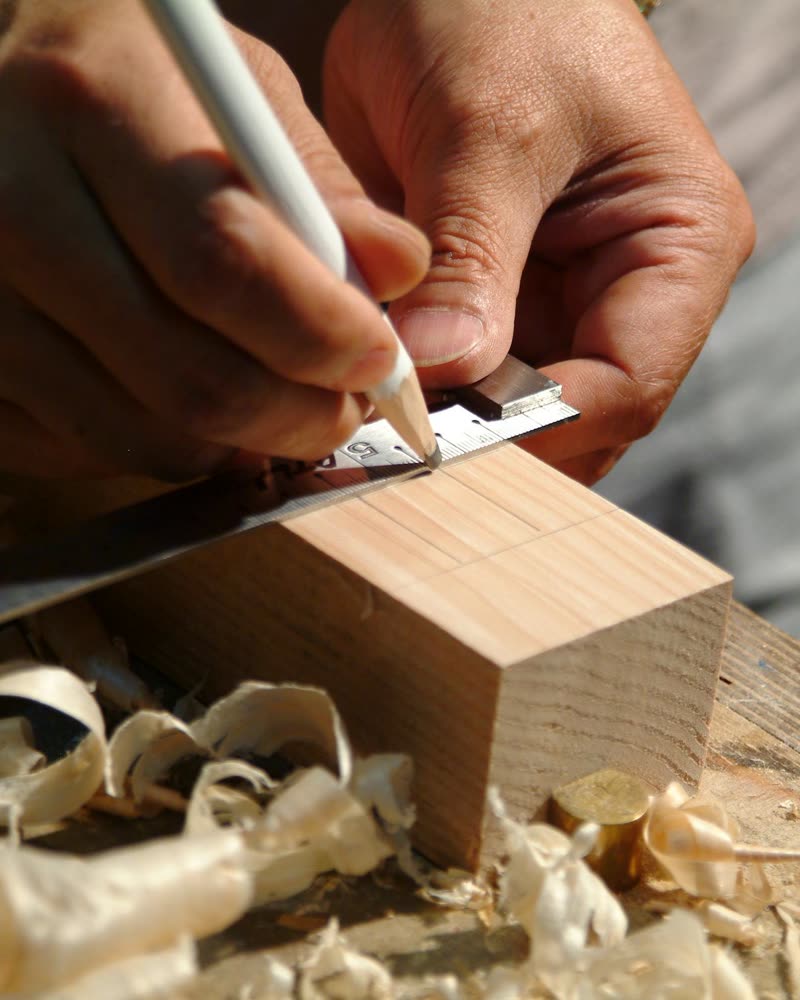 A tradie's hands marking a pencil line on a timber off-cut, wood shavings on the bench