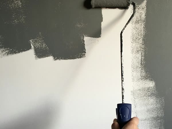 A hand pushing a paint roller up a wall, mid-stroke