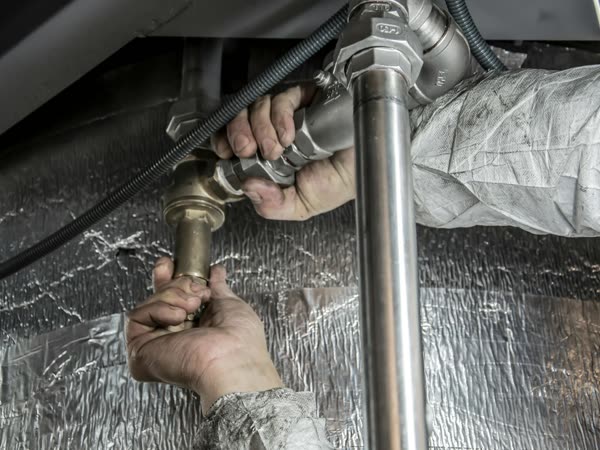 A plumber's hands tightening brass fittings on copper pipe under a sink
