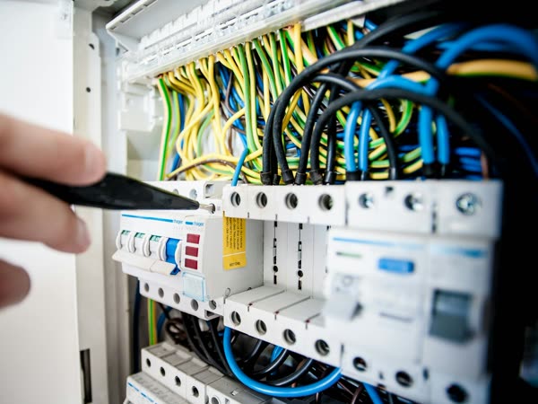An electrician's hand with a screwdriver on a circuit breaker switchboard with colored wires